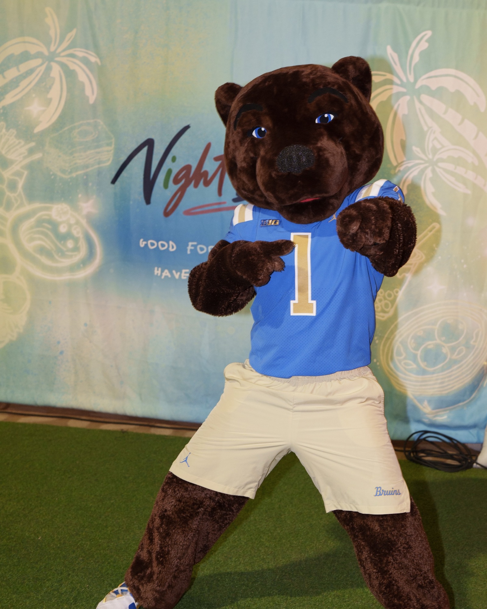 A bear mascot posing in front of the NightBite backdrop